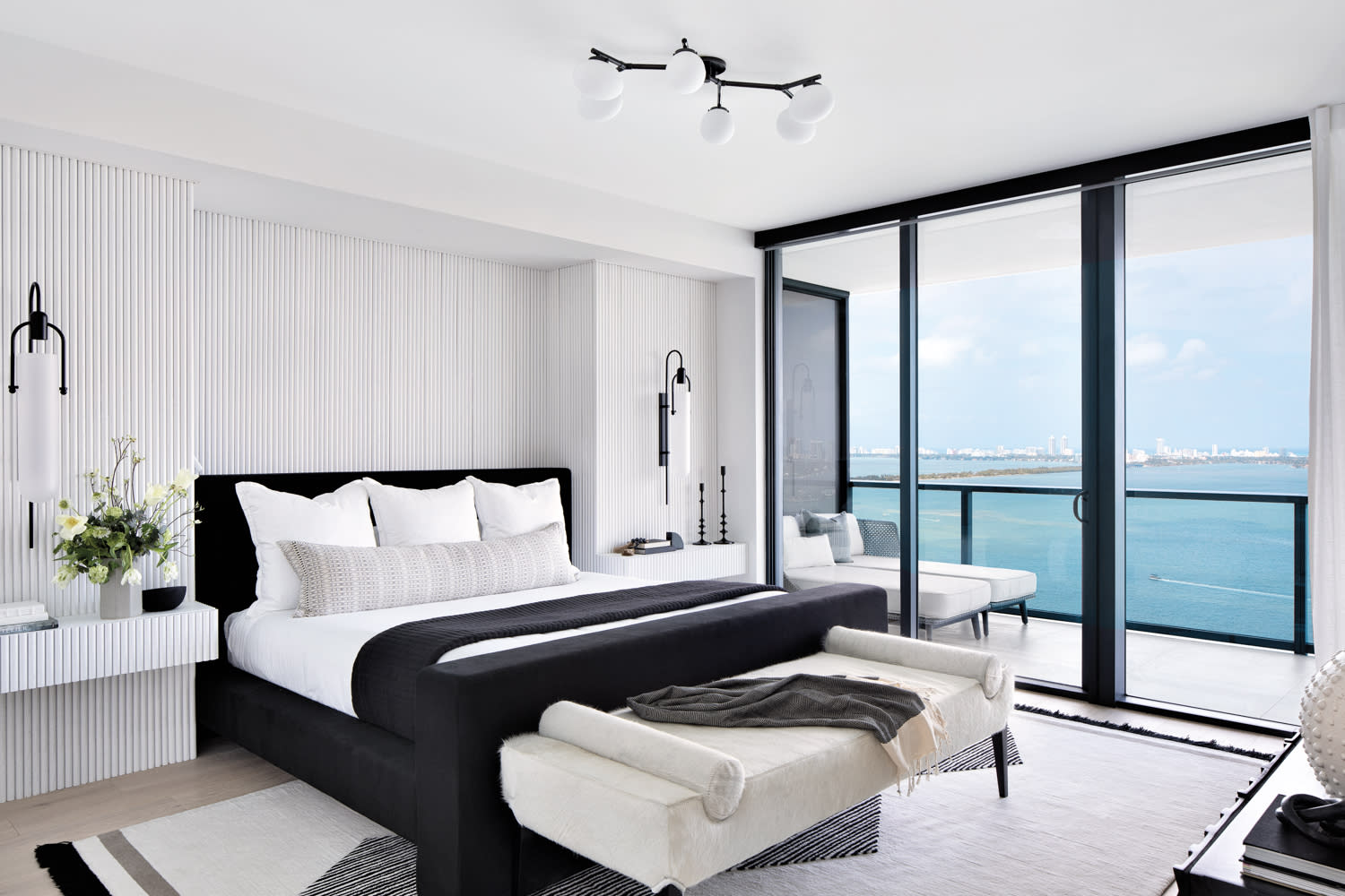 primary bedroom with white walls, black bed, white bench and window wall