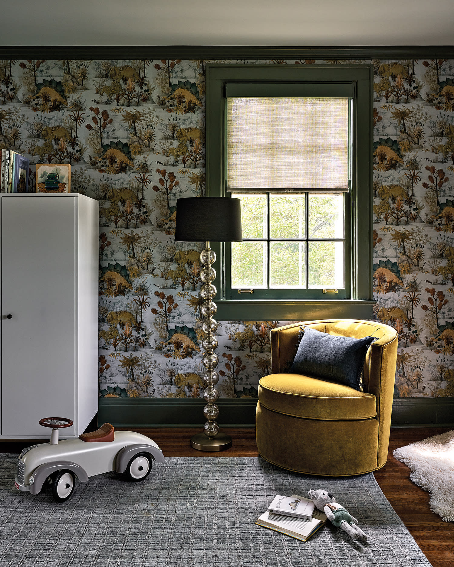 boy's bedroom with dinosaur-themed wallpaper, play car and a yellow swivel chair