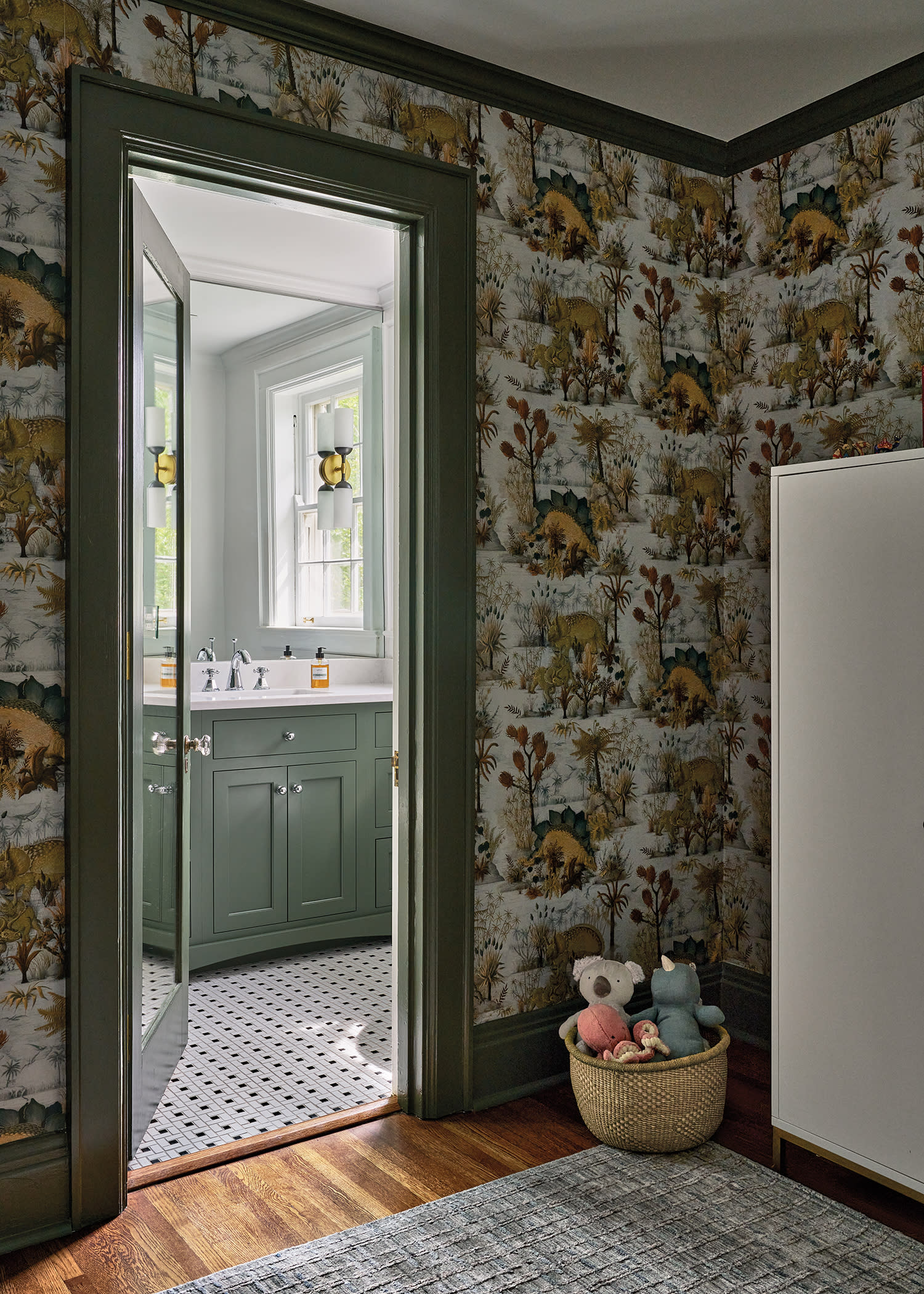 vintage-inspired dinosaur wallpaper surrounds a bedroom leading into a bathroom with a green vanity