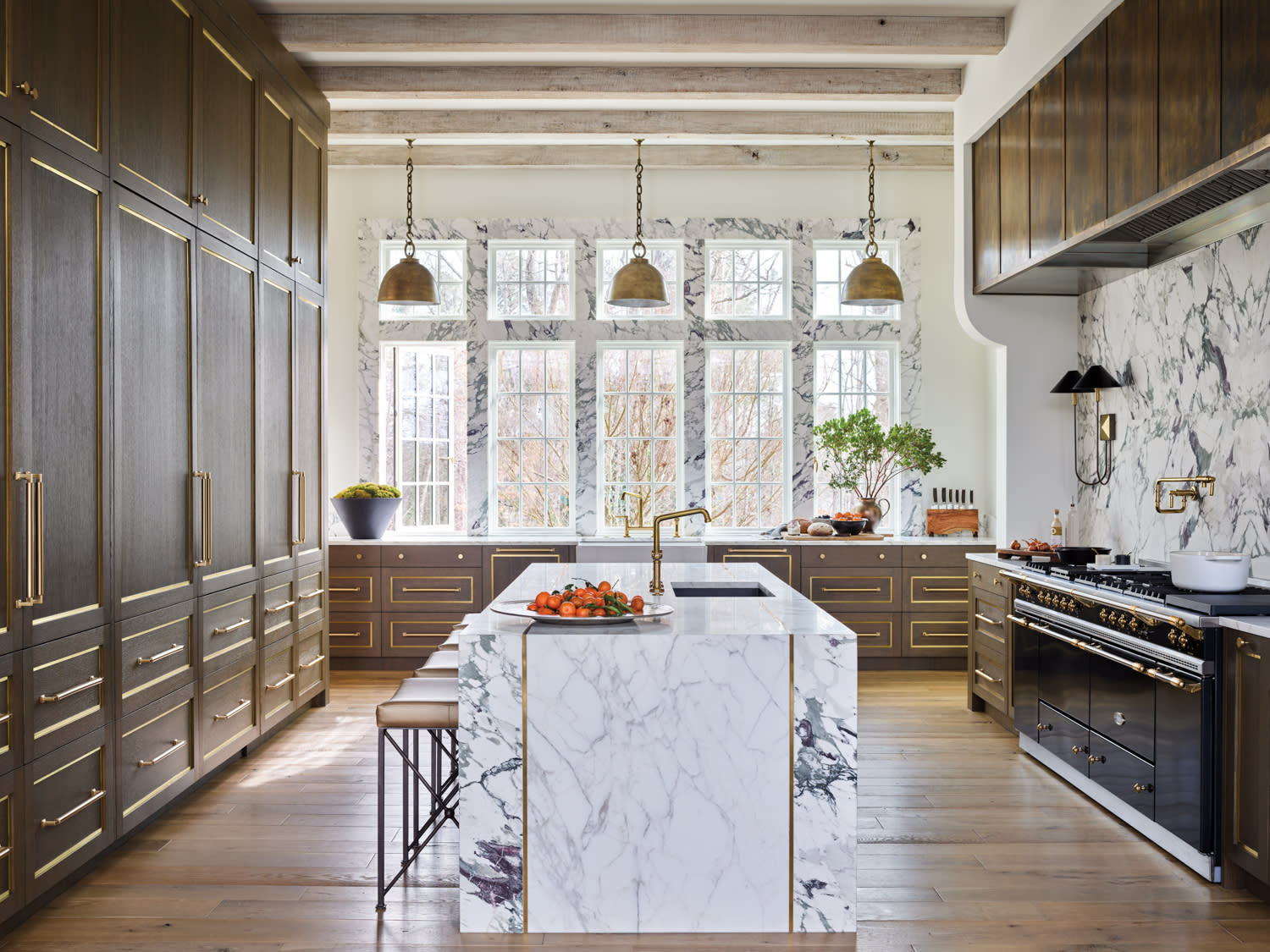 Kitchen featuring dramatic slabs of marble, brass detailing and three matching pendant lights by Amy Morris